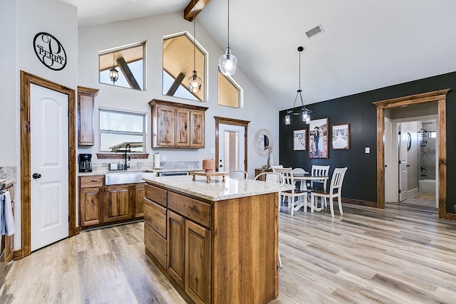 kitchen featuring light stone counters, a sink, a center island, brown cabinetry, and decorative light fixtures