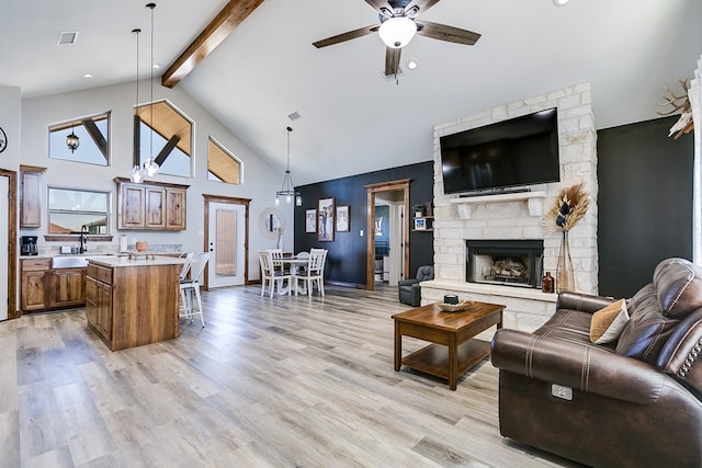 living area with ceiling fan, high vaulted ceiling, a stone fireplace, light wood-style flooring, and beam ceiling