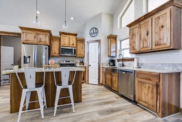 kitchen with stainless steel appliances, a center island, brown cabinets, light stone countertops, and decorative light fixtures