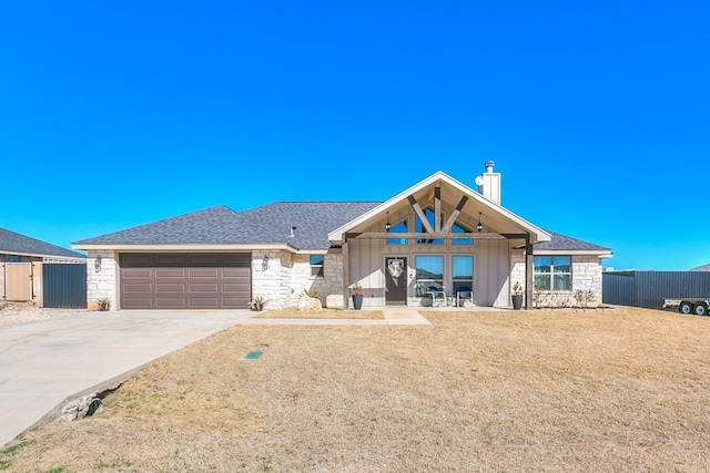 view of front facade featuring driveway, stone siding, a chimney, an attached garage, and fence