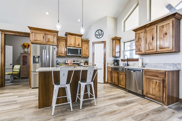 kitchen with light stone countertops, stainless steel appliances, a sink, a kitchen island, and brown cabinets