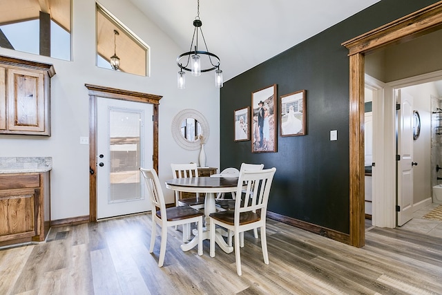 dining space with baseboards, high vaulted ceiling, and light wood-style floors