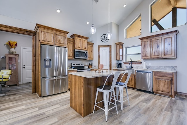 kitchen with stainless steel appliances, a kitchen island, light wood-style floors, hanging light fixtures, and brown cabinets