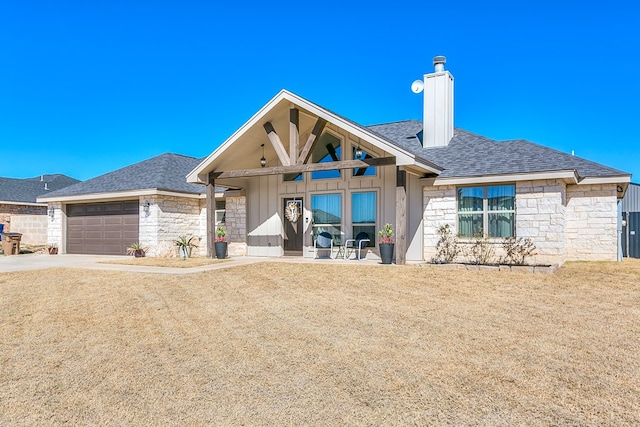 view of front facade featuring board and batten siding, a front yard, stone siding, and an attached garage