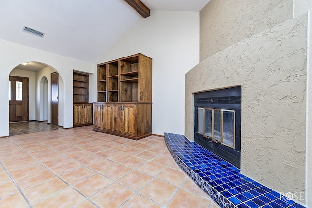 unfurnished living room with arched walkways, high vaulted ceiling, visible vents, beamed ceiling, and a glass covered fireplace