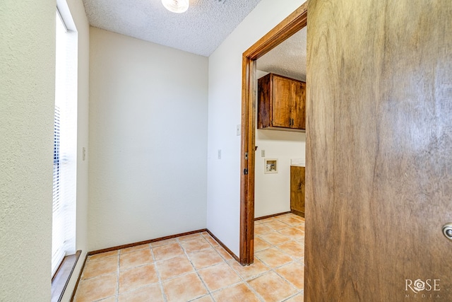 corridor with light tile patterned floors, baseboards, and a textured ceiling