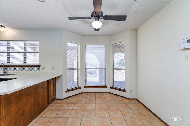 kitchen with light countertops, light tile patterned flooring, ceiling fan, a textured ceiling, and a sink