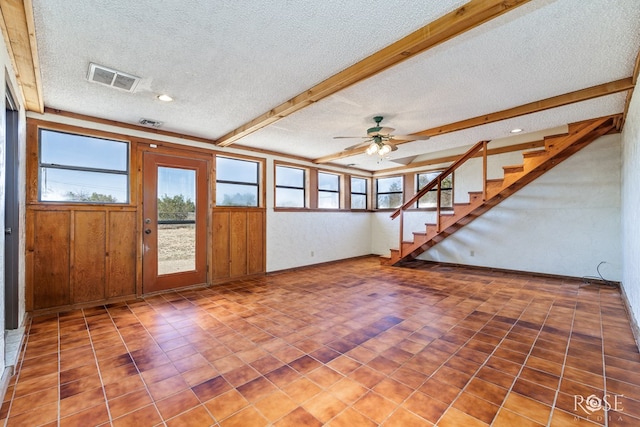 unfurnished living room featuring visible vents, ceiling fan, stairway, beamed ceiling, and a textured ceiling