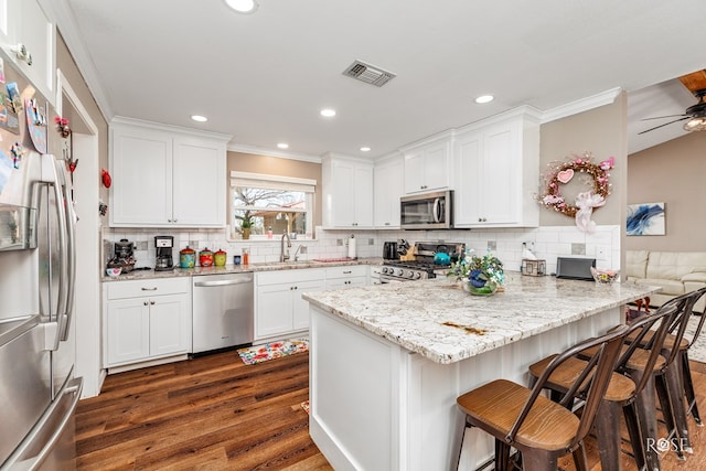 kitchen featuring sink, a breakfast bar area, white cabinetry, stainless steel appliances, and light stone counters