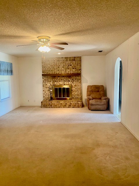 8882 Fm 765, San Angelo, TX 76905 - unfurnished living room with carpet floors, ceiling fan, arched walkways, a textured ceiling, and a brick fireplace
