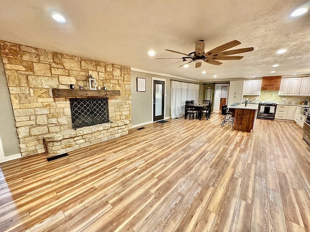 unfurnished living room with ceiling fan, a fireplace, ornamental molding, and a textured ceiling