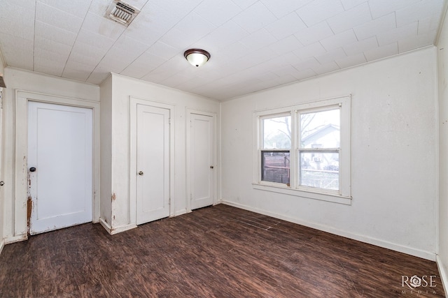 unfurnished bedroom featuring dark wood-style floors, visible vents, and baseboards