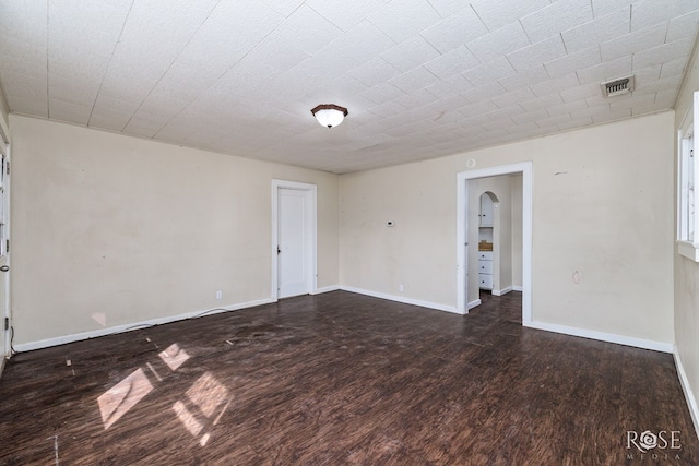 unfurnished room featuring arched walkways, visible vents, wood finished floors, and baseboards