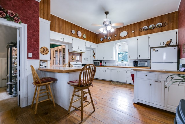 kitchen with white refrigerator, a breakfast bar, kitchen peninsula, and white cabinets