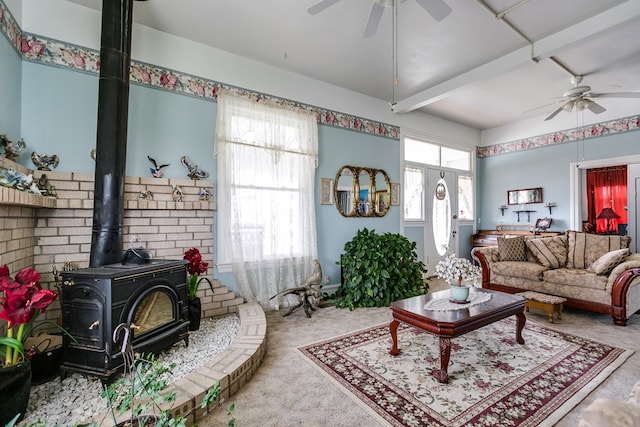 carpeted living room with beam ceiling, ceiling fan, and a wood stove