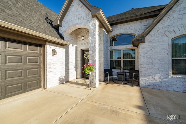 entrance to property featuring driveway, stone siding, brick siding, and an attached garage