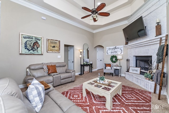 carpeted living area with baseboards, a tray ceiling, arched walkways, ceiling fan, and a brick fireplace