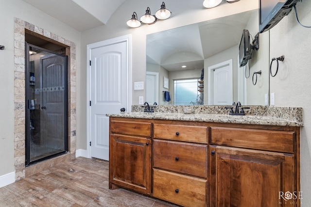 bathroom with double vanity, wood finished floors, a stall shower, and a sink