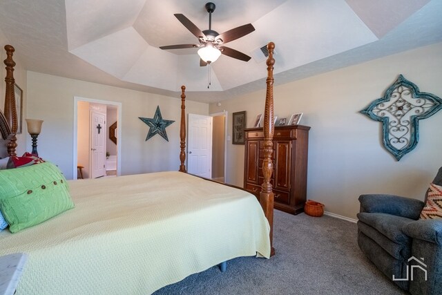 carpeted bedroom with ensuite bath, ceiling fan, and a tray ceiling