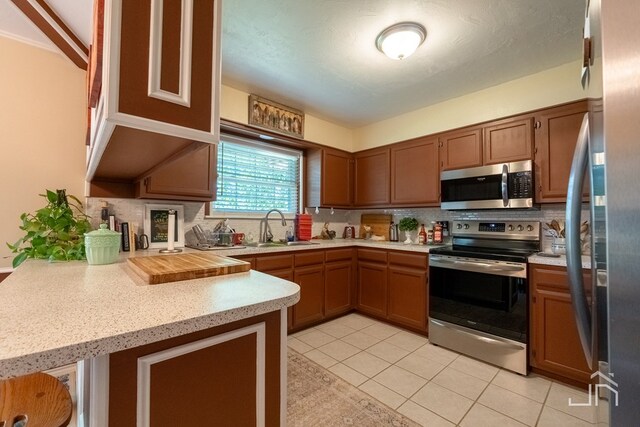 kitchen featuring sink, backsplash, light tile patterned floors, kitchen peninsula, and stainless steel appliances