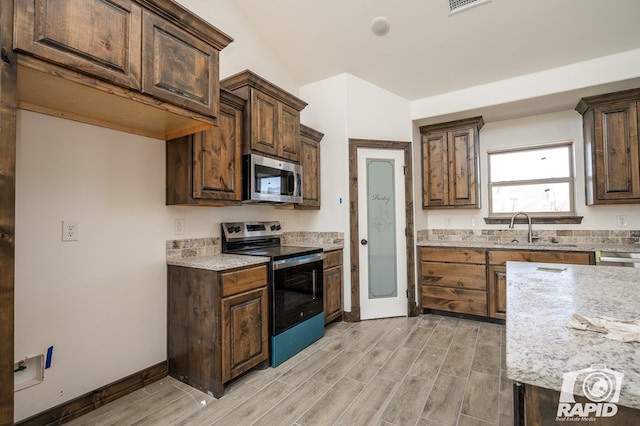 kitchen featuring wood finish floors, appliances with stainless steel finishes, a sink, dark brown cabinets, and baseboards