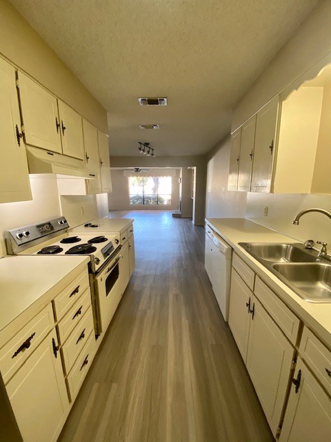 kitchen with under cabinet range hood, white appliances, a sink, white cabinetry, and visible vents