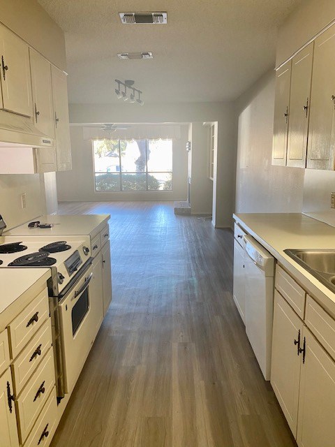 kitchen featuring light countertops, visible vents, open floor plan, white appliances, and under cabinet range hood