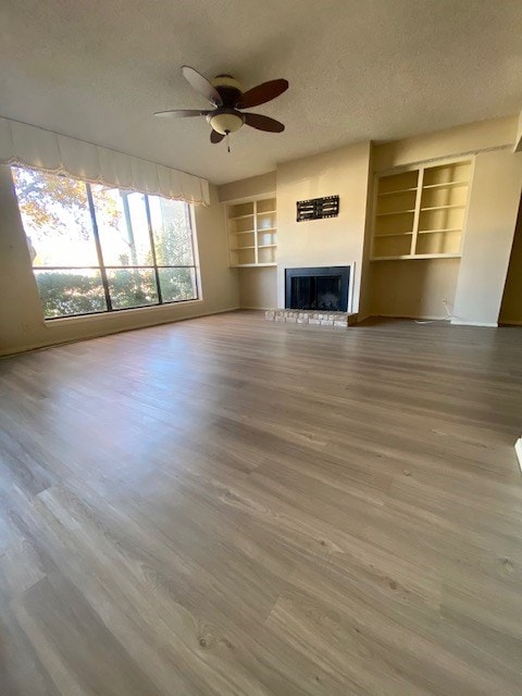 unfurnished living room featuring built in shelves, a fireplace with raised hearth, a textured ceiling, and wood finished floors