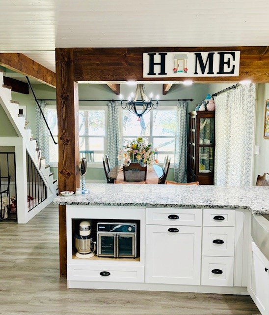 kitchen featuring an inviting chandelier, light wood-style floors, light stone countertops, and white cabinetry