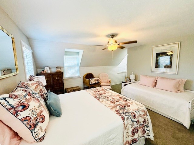 carpeted bedroom with a ceiling fan, vaulted ceiling, and multiple windows