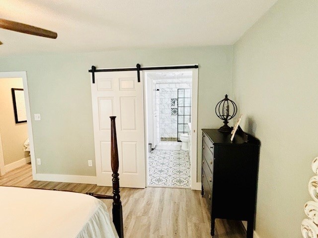 bedroom with ensuite bath, baseboards, light wood finished floors, and a barn door