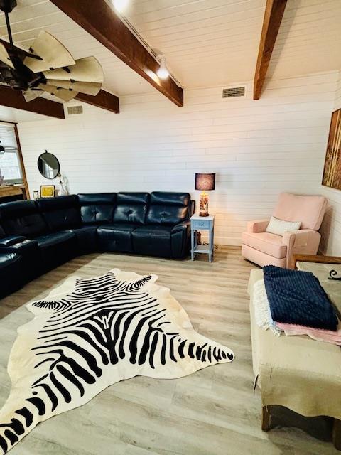 living room with beamed ceiling, wood walls, wood finished floors, and visible vents