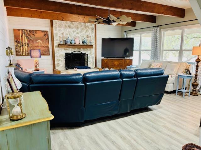 living room featuring wood finished floors, wooden walls, a fireplace, and beamed ceiling