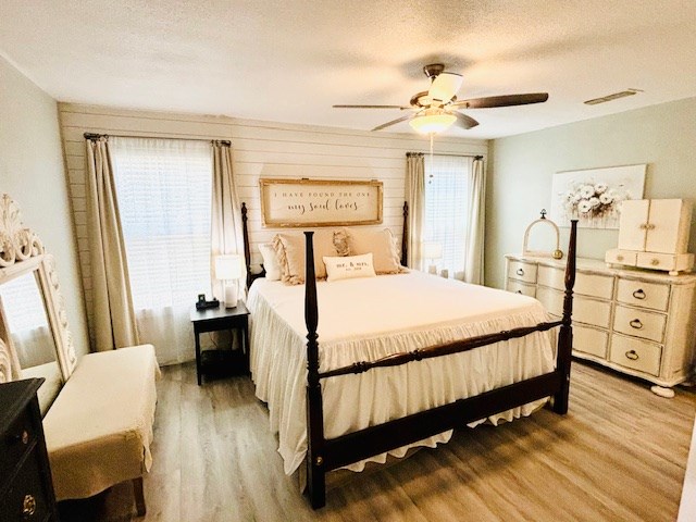 bedroom with a ceiling fan, light wood finished floors, a textured ceiling, and visible vents