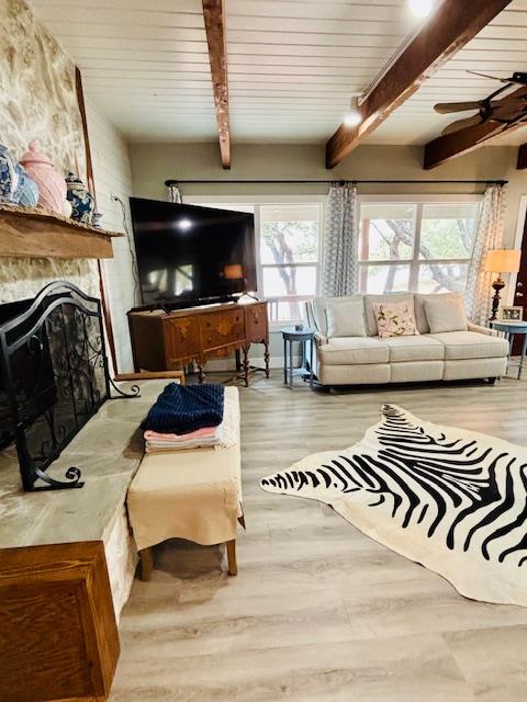 living area featuring ceiling fan, plenty of natural light, beamed ceiling, and wood finished floors