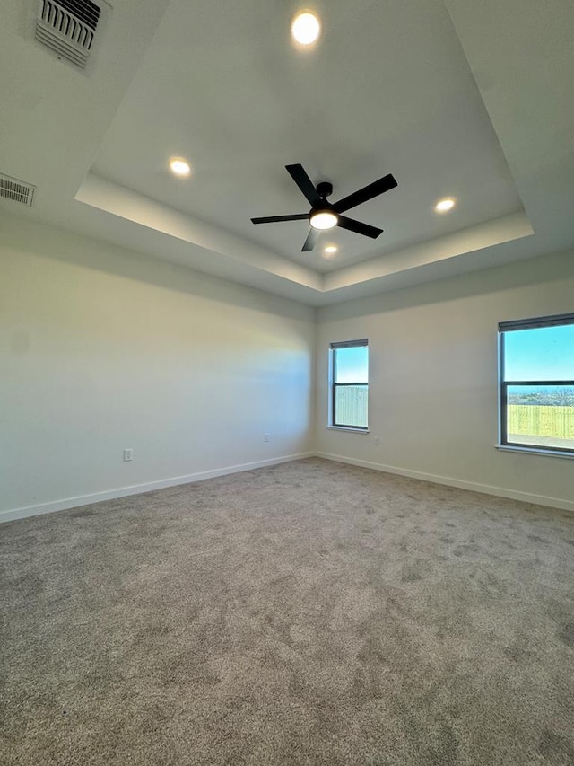 carpeted empty room with baseboards, visible vents, and a raised ceiling