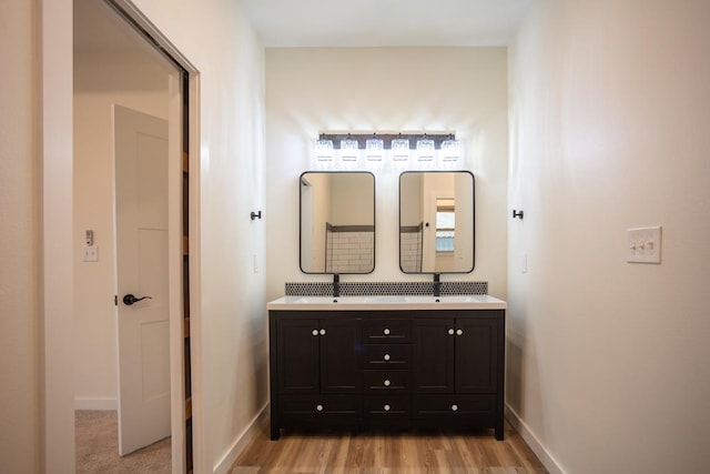 bathroom with baseboards, double vanity, and wood finished floors