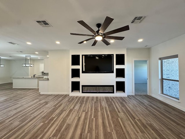 unfurnished living room with ceiling fan, visible vents, and wood finished floors