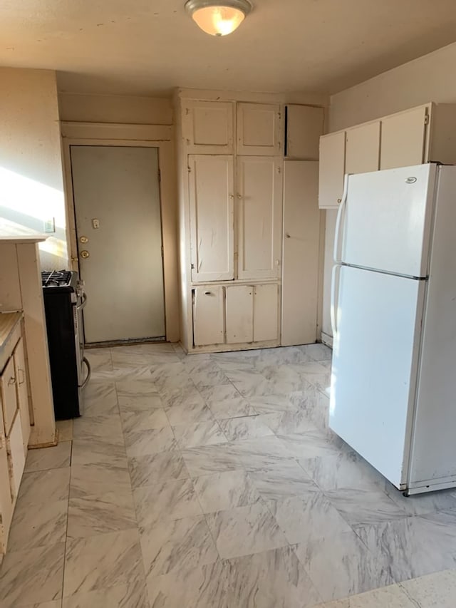 606 Pulliam St, San Angelo, TX 76903 - kitchen with freestanding refrigerator, stainless steel range with gas cooktop, white cabinetry, and light marble finish flooring