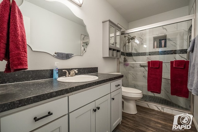 bathroom with vanity, toilet, wood finished floors, and a stall shower