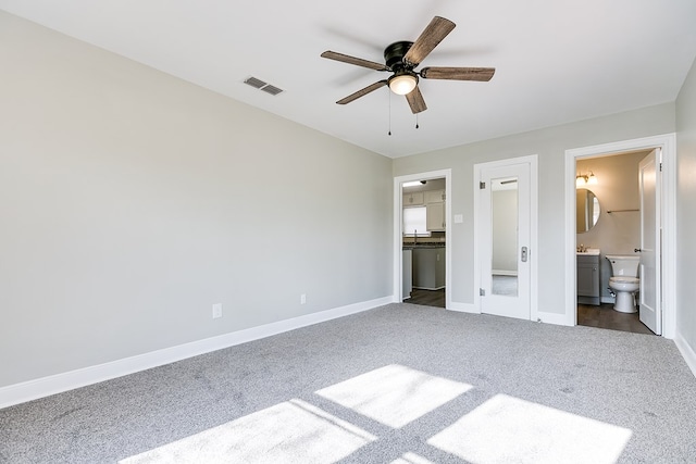 unfurnished bedroom featuring connected bathroom, visible vents, baseboards, dark carpet, and a walk in closet