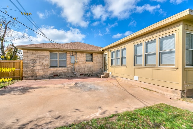 rear view of house with stone siding, crawl space, a patio, and fence