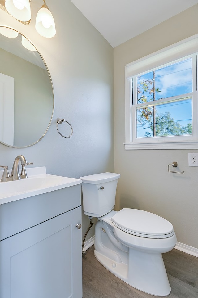 half bath with toilet, baseboards, wood finished floors, and vanity