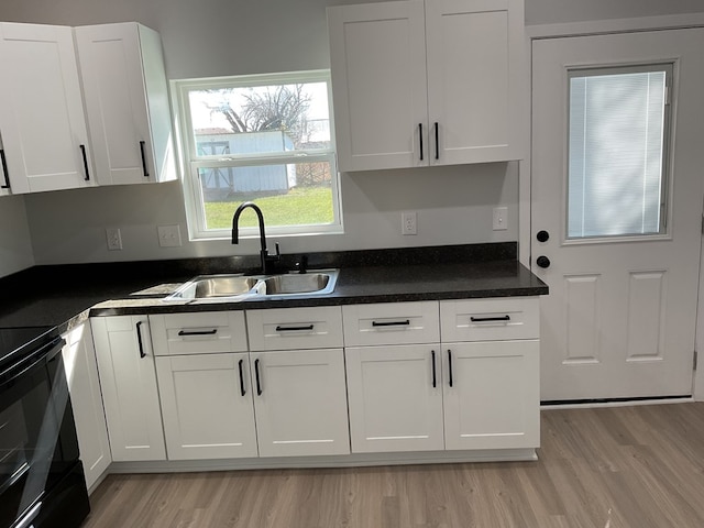 kitchen with white cabinetry, sink, light hardwood / wood-style floors, and black / electric stove