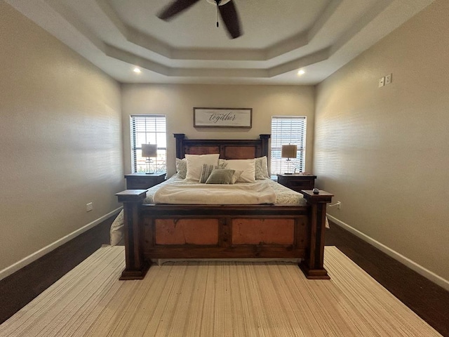 bedroom with a tray ceiling, wood-type flooring, and ceiling fan