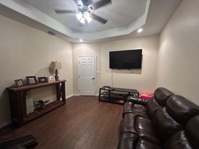 living room with a raised ceiling, dark wood-type flooring, and ceiling fan