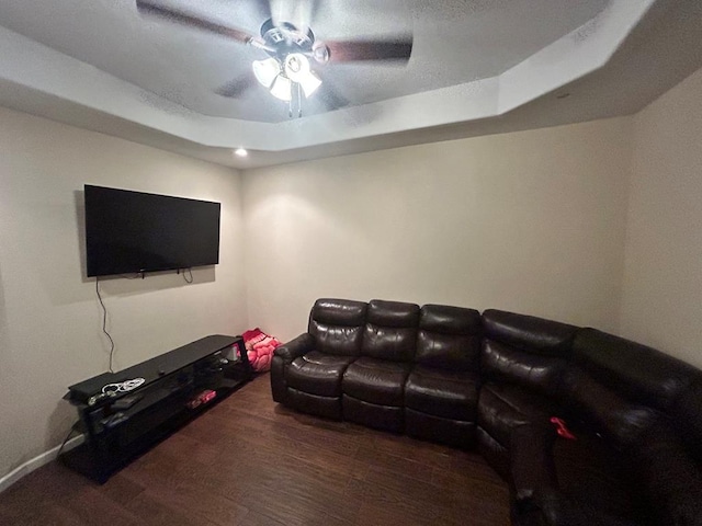 living room with dark wood-type flooring, ceiling fan, and a tray ceiling