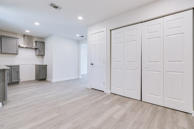 2624 Dallas St, San Angelo, TX 76903 - kitchen with wall chimney exhaust hood, gray cabinetry, decorative backsplash, light wood-type flooring, and light stone countertops