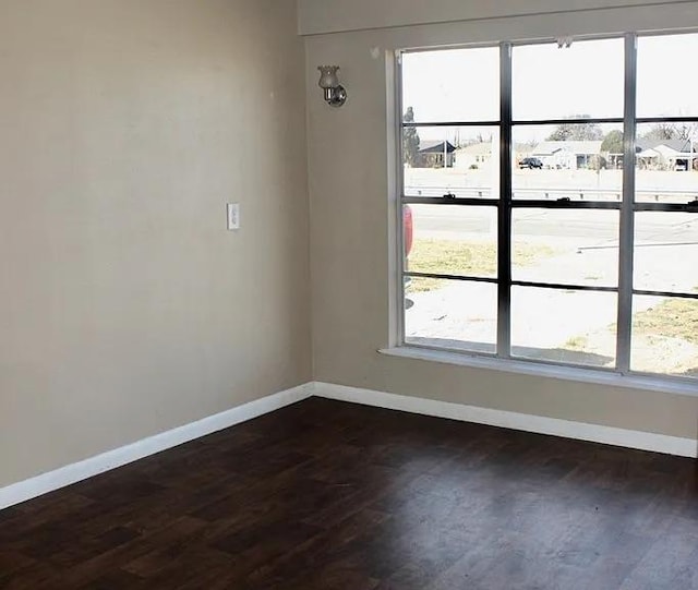 empty room featuring baseboards, a healthy amount of sunlight, and dark wood-style flooring