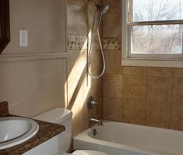 full bath with bathtub / shower combination, toilet, vanity, and a wainscoted wall